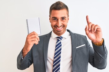 Young handsome business man holding blank notebook over isolated background surprised with an idea or question pointing finger with happy face, number one