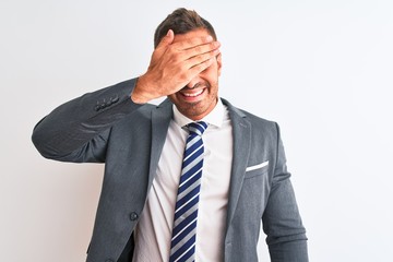 Young handsome business man wearing suit and tie over isolated background smiling and laughing with hand on face covering eyes for surprise. Blind concept.