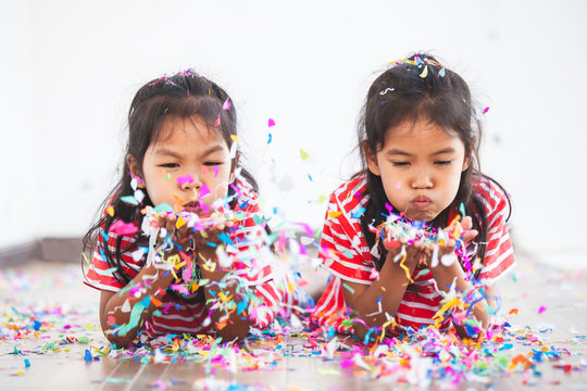 Cute asian child girl and her sister play with colorful confetti together to celebrate in their party with fun