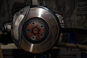 A close-up on the brake system of a car with pads, discs, a caliper on a lift in a vehicle repair workshop. Auto service industry.