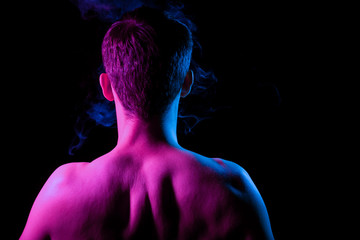 Close-up of nape, back and shoulders with strained muscles of an short hair head of a man with stubble, naked without clothes, illuminated in blue and pink on a black isolated background with smoke