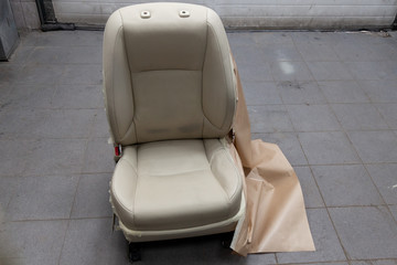 One sport seats with beige leather trim, located on the floor in the workshop for repair and tuning of cars and vehicles. Auto service industry.
