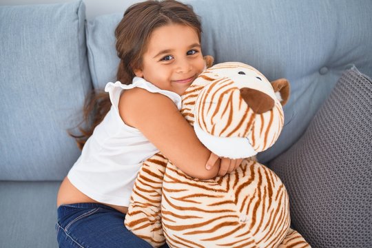 Adorable toddler smiling happy. Sitting on the sofa hugging doll at home