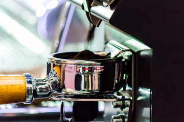 Espresso machine grinding roasted coffee bean into tamper. .