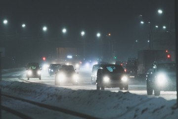 snowy winer night on a road with traffic in a city with lots of lights and billboards in the street