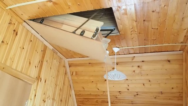 Opening the attic hatch in a new wooden house. Get the ladder to the attic in the hatch on the ceiling.