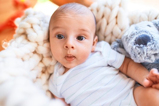 Adorable baby lying down over blanket on the floor at home. Newborn relaxing and resting comfortable with teddy bear