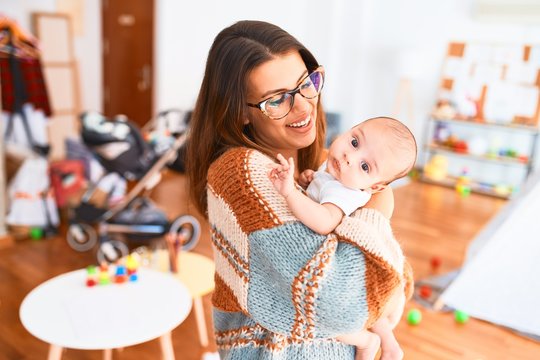 Young beautiful woman and her baby standing at home. Mother holding and hugging newborn