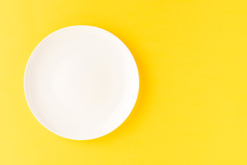 Overhead shot of blank white plate on yellow background. Flat lay