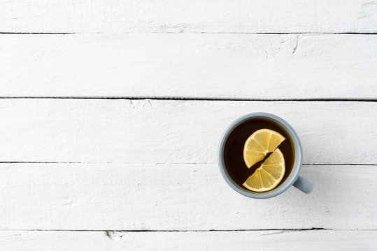 Cup of tea with silce of lemon on white wooden table. Top view