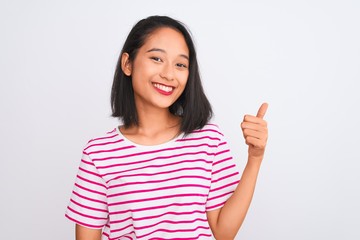 Young chinese woman wearing striped t-shirt standing over isolated white background doing happy thumbs up gesture with hand. Approving expression looking at the camera showing success.