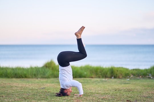 Young beautiful sportwoman practicing yoga. Coach teaching headstand pose at park