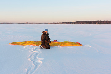 Fototapeta na wymiar Man sitting next to an orange kite putting on a mitten, Ob reservoir, Novosibirsk, Russia