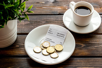 Pay restaurant bill by cash. Reciept and coins on plate on dark wooden background
