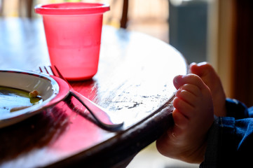 Young Caucasian child with feet resting on the edge of a kitchen table with a fork, cup, and plate visible