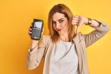 Redhead caucasian business woman holding point of sale terminal over isolated background with angry...