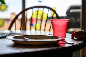 Young toddler with hand resting on table next to a red cup, plate, and fork