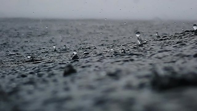 Rain drops into the endless ocean, close up. It briefly bounces back to the air after it hits the sea surface, slow motion.