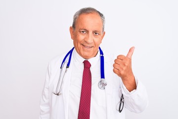 Senior grey-haired doctor man wearing stethoscope standing over isolated white background doing happy thumbs up gesture with hand. Approving expression looking at the camera showing success.