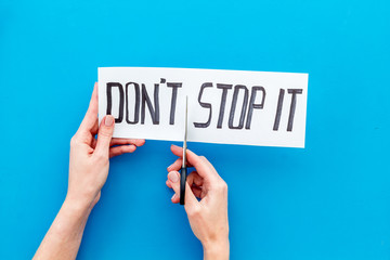 Encouragement and motivation. Hands cutting text Don't stop it with scissors on blue desk