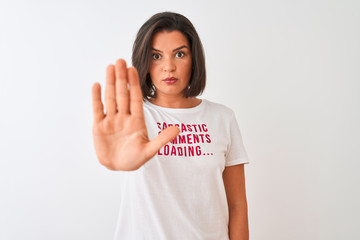 Young beautiful woman wearing fanny t-shirt standing over isolated white background with open hand doing stop sign with serious and confident expression, defense gesture