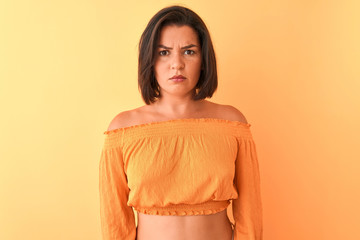 Young beautiful woman wearing casual t-shirt standing over isolated orange background skeptic and...