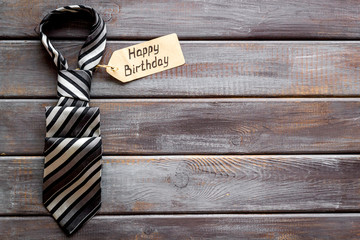 Fototapeta premium Man's birthday concept. Happy birthday text near men's tie on dark wooden background top view copy space