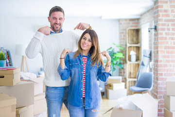Fototapeta premium Young beautiful couple standing at new home around cardboard boxes looking confident with smile on face, pointing oneself with fingers proud and happy.