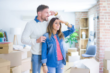 Young beautiful couple standing at new home around cardboard boxes very happy and smiling looking...