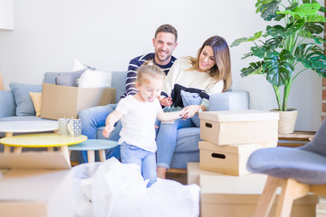 Fototapeta na wymiar Beautiful family, parents sitting on the sofa drinking coffee looking his kid playing at new home around cardboard boxes
