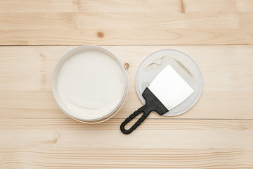 Spatula and a bucket of white putty on wooden boards. Top view Copy space.