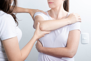 Doctor physiotherapist assisting a woman patient while giving exercising treatment massaging the arm of patient in a physio room. Rehabilitation physiotherapy concept.
