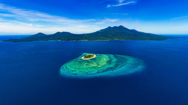 Beautiful Mantigue island with the volcanic Camiguin Island resting behind it while it dwells in the vibrant blue waters of the Philippines.