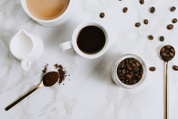 Flatlay of fresh cups of espresso and milk coffee, creamer, coffee beans and spoon on marble...