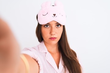 Girl wearing pajama and sleep mask make selfie by camera over isolated white background with a...