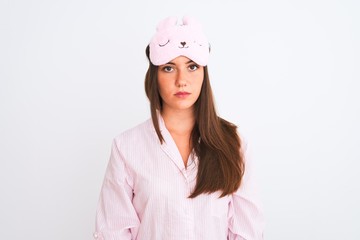 Young beautiful girl wearing pajama and sleep mask standing over isolated white background with...