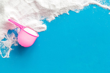 Washing powder in plastic spoon on blue background top view copy space