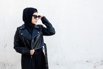 Naklejka premium Portrait of beautiful middle-eastern girl in traditional Islamic clothing - hijab. Modern and young Iranian woman in sunglasses and a leather jacket