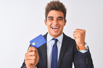 Young handsome businessman wearing suit holding credit card over isolated white background screaming proud and celebrating victory and success very excited, cheering emotion