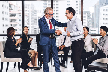 Image two business partners in elegant suit successful handshake together standing in front of group of casual business clapping hands in modern office.Partnership approval and thanks gesture concept