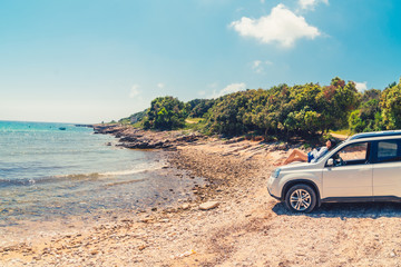 woman sitting on car hood at summer beach vacation concept