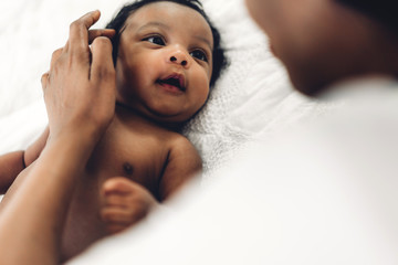 African american mother playing with adorable little african american baby in a white bedroom.Love...