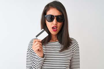 Fototapeta premium Young chinese woman wearing sunglasses holding credit card over isolated white background scared in shock with a surprise face, afraid and excited with fear expression