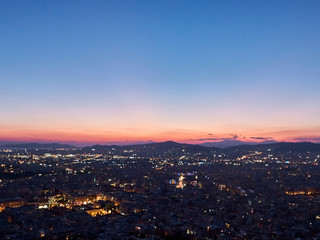 Fototapeta na wymiar City panorama at sunset. Dusk landscape with city, mountains and clouds in the rays of setting sun. Athens, Greece