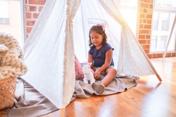 Beautiful toddler girl sitting on the floor playing with unicorn inside tipi at kindergarten © Krakenimages.com