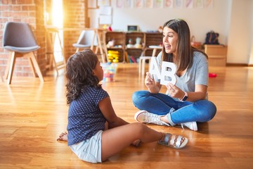 Beautiful teacher teaching alphabet to student toddler girl at kindergarten