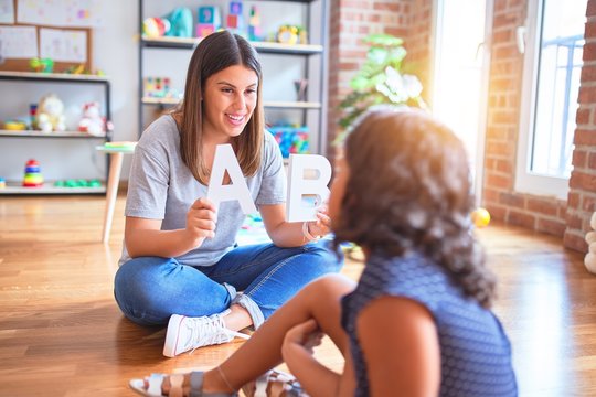 Beautiful teacher teaching alphabet to student toddler girl at kindergarten