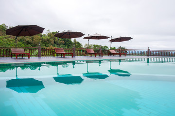 Swimming pool with wooden bench or chair and umbrella.