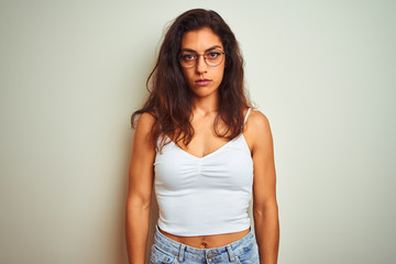 Young beautiful woman wearing t-shirt and glasses standing over isolated white background with serious expression on face. Simple and natural looking at the camera.