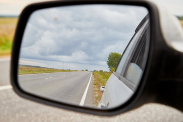 The reflection of road in the side view mirror in autumn day. Travel concept